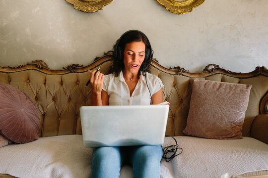 Woman working on laptop with headphones on elegant sofa