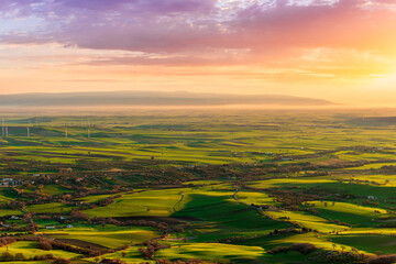 Fototapeta premium beautiful panoramic landscape of green valley fielis and hills during spring sunet or sunrise with agricultural farms and colorful cloudy sunset on background