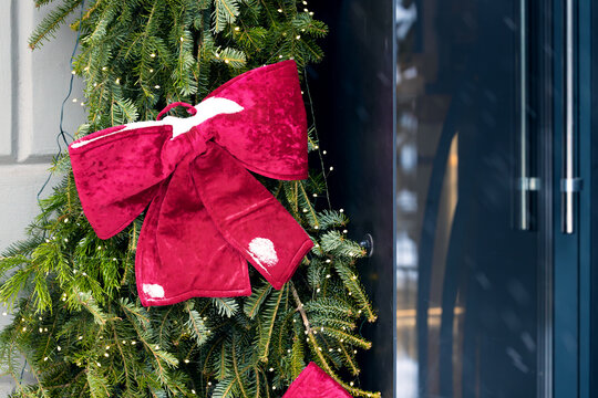 large red velvet bow adorns a festive evergreen branch decorated with lights for the holidays
