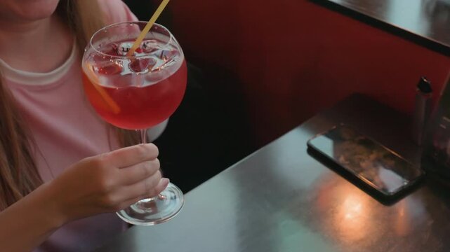 Two women enjoy red cocktails at table in casual dining setting interacting with drinks and each other. Table features smartphone condiment holder menu stand soft lighting creates warm