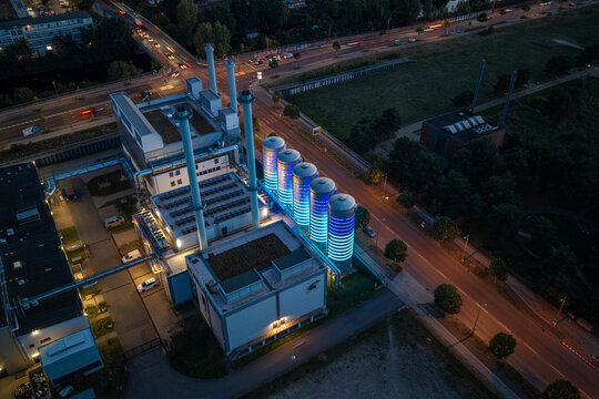 Aerial view of the BTB Heat and Power Plant Adlershof with glowing thermal storage tanks illuminating the industrial facility at night in Berlin, Berlin, Germany.