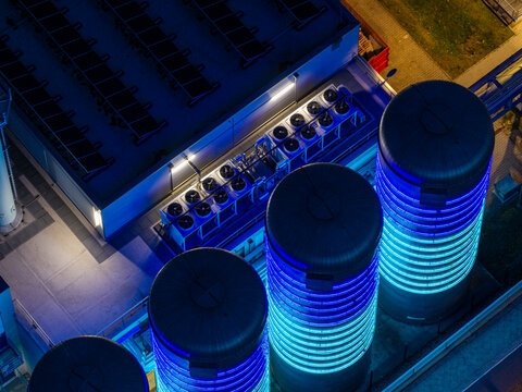 Aerial view of the BTB Heat and Power Plant Adlershof at night, with glowing blue thermal storage tanks visualizing heat energy and industrial cooling units in Berlin, Berlin, Germany.