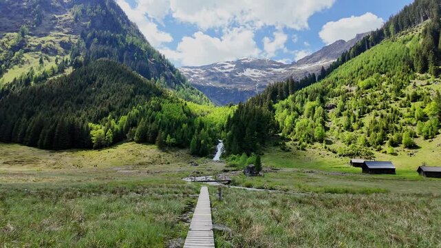 Wooden path through marshy terrain to river. Mountain landscape with waterfall river. Mountain landscape bridge path. Village landscape. Picturesque valley with waterfall coming down from mountain