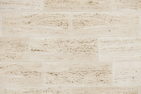 Light beige textured stone wall with horizontal rectangular panels and porous natural surface detail for architectural backgrounds and interior design materials