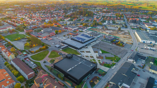 Aerial view of a modern black building complex with a water slide, surrounded by parking areas, residential houses, and autumn trees in a town in Sweden.