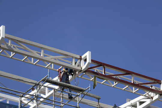 Construction worker safety harness steel beam scaffolding blue sky industrial structural daytime architecture engineering. Construction worker wearing safety harness working steel beam