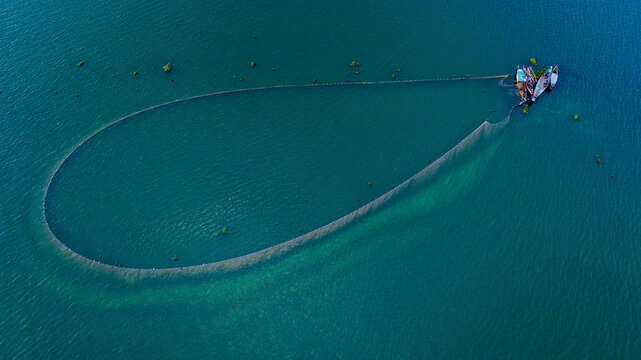 Aerial view of traditional fishing nets arranged in a large loop in the clear blue waters of Kaptai Lake with small wooden boats nearby in Rangamati, Chittagong Division, Bangladesh.
