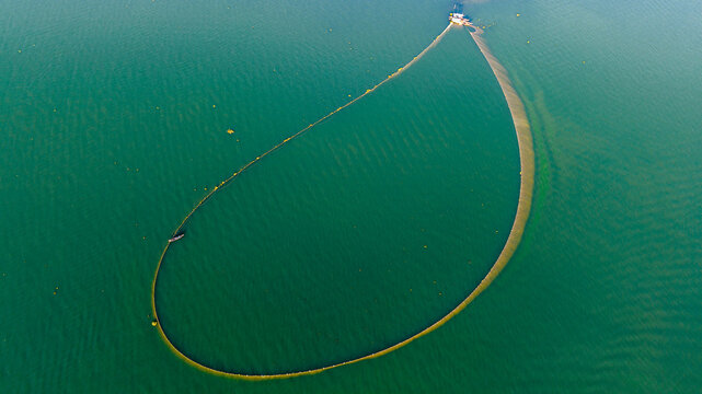 Aerial view of a fishing net forming a large loop in the green waters of Kaptai Lake with a small boat in Rangamati, Chittagong Division, Bangladesh.