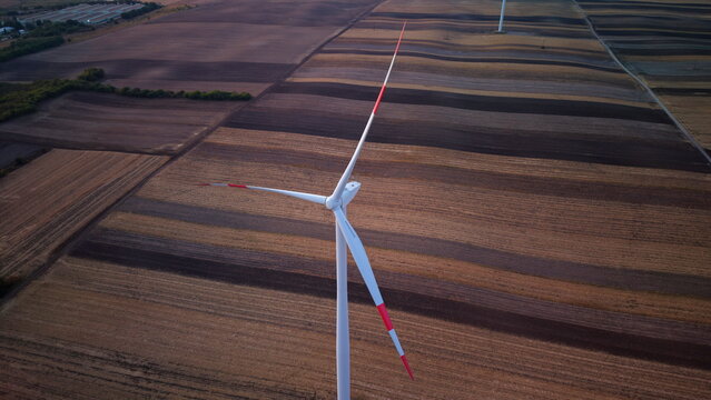 Aerial view of a wind turbine standing in a vast agricultural field with striped patterns of tilled soil in Vladimirovac, Vojvodina, Serbia.
