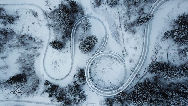 Aerial view of the Col de la Faucille summer sledge track covered in snow, winding through a dense pine forest in the Jura mountains, Gex, Auvergne-Rhone-Alpes, France.