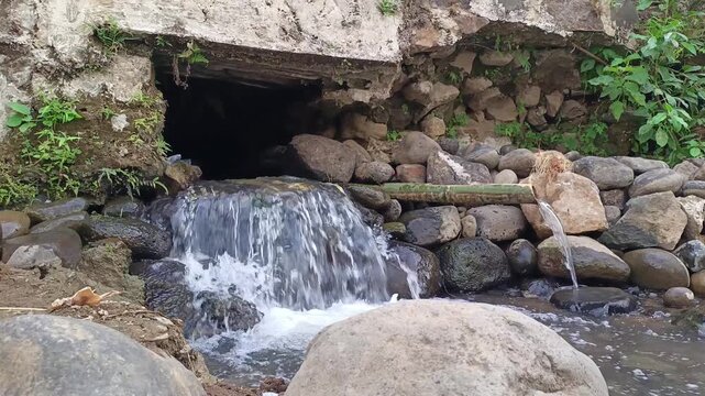 Clean water flowing continuously from a concrete culvert tunnel into a rocky river stream