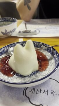 White cat-shaped panna cotta dessert. A white jelly-like dessert shaped like a cat sits on a plate as it is shaken, wobbling and gently jiggling.