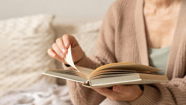 Woman reads book, turns page, and enjoys her leisure time indoors. Cozy moment of reading and self-education. Concept of slow and mindful living