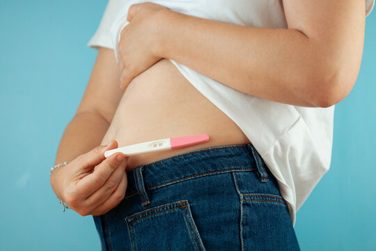 woman holding pregnancy test near bare belly white shirt jeans blue background pregnancy announcement concept of family motherhood fertility healthcare