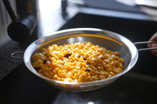 Corn and red beans draining in metal strainer over kitchen sink