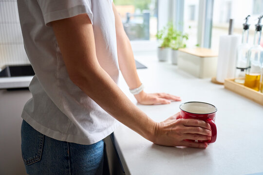 Woman standing at kitchen countertop with hand holding red mug