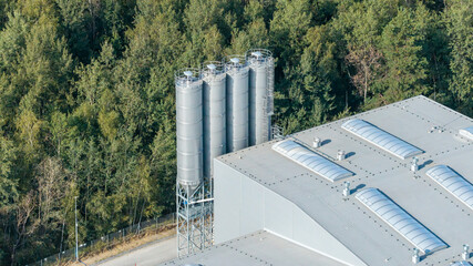 Industrial manufacturing plant with storage silos next to green forest, aerial view © Marcin