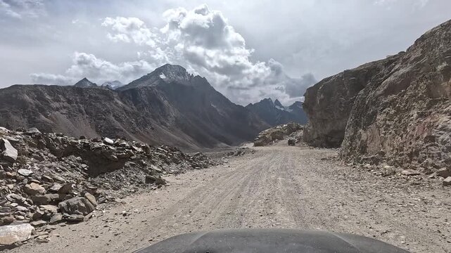 A vehicle drives along an unpaved gravel road cut through shattered rock between towering jagged mountain peaks with glacie - Spiti Valley Himachal Pradesh India | Himalayan road trip GoPro dashcam 4K