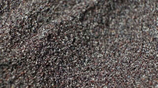 Spreading ground poppy seeds to show crumbly dry texture macro shot.