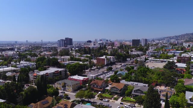 Aerial panorama of residential houses, streets, apartment complexes, and distant commercial towers in Hollywood, Los Angeles, California, under a clear cloudless sky.