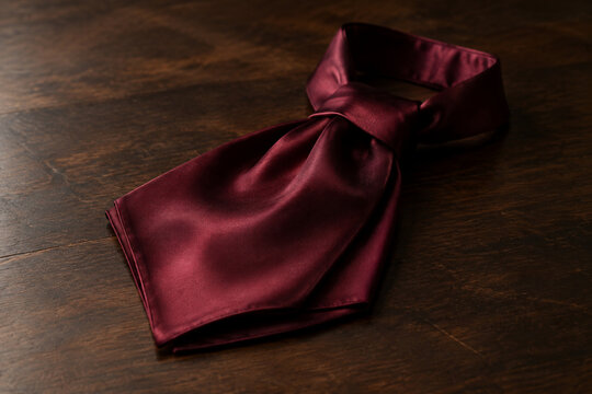 Folded burgundy silk cravat on dark wood, elegant menswear and formal fashion concept