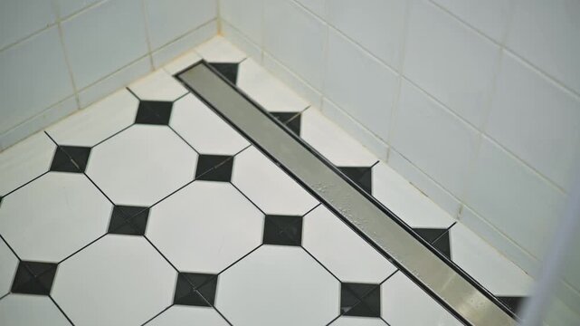 close-up view of a shower floor featuring alternating black and white octagonal tiles. A metal drainage channel is visible along the edge, highlighting the tile pattern and design