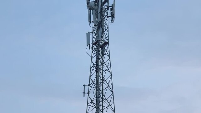 Low angle wide tilt up view of a tall telecommunications tower with multiple cellular antennas and steel lattice framework against a clear blue sky