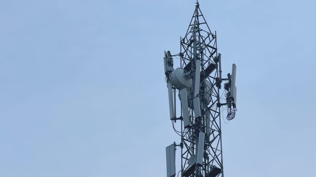 Smooth panning shot across a telecommunications cell tower showing multiple cellular antennas and communication equipment mounted on a steel lattice structure