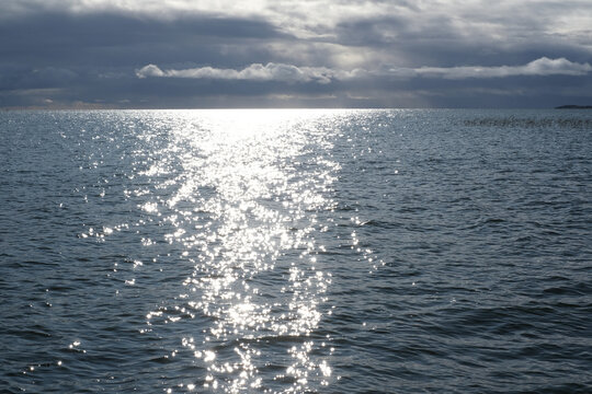 Bright sun reflection shimmering on the calm sea surface under a dramatic cloudy sky