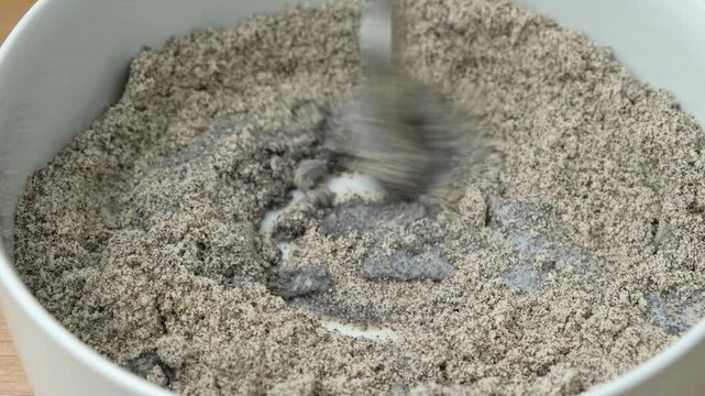 Mixing poppy seed filling with milk in bowl with spoon close up