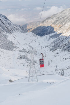 View of a red cable car traveling over a snow-covered mountain valley with support towers along the Transfagarasan in Curtea de Arges, Judetul Arges, Romania.