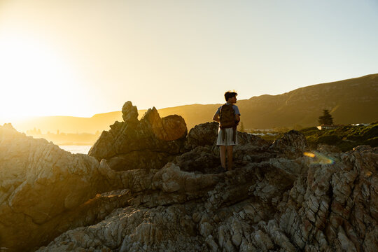 13 year old boy wearing backpack exploring the iconic rocky coastline of Kammabaai Beach, Hermanus, South Africa at sunset
