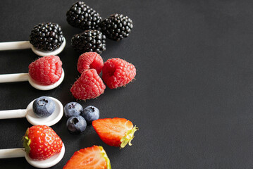 Fresh mixed berries on white spoons over dark background with space for text © Наталья Бабак