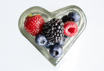 Fresh organic berries in a heart shaped glass bowl on white background. isolated © Наталья Бабак