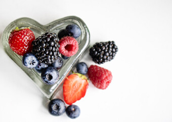 Fresh organic berries in a heart shaped glass bowl on white background. © Наталья Бабак
