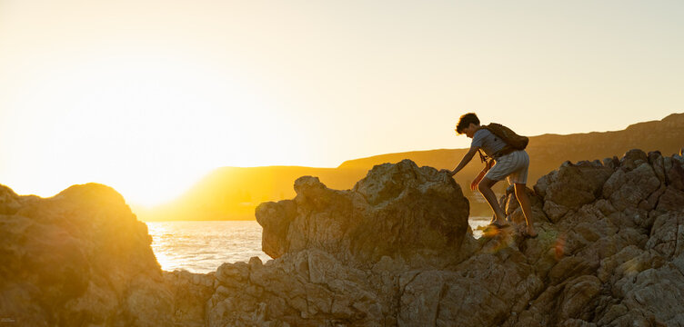 13 year old boy wearing backpack exploring the iconic rocky coastline of Kammabaai Beach, Hermanus, South Africa at sunset