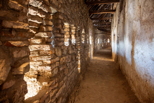 View of the historic stone walkway inside the Prejmer Fortified Church, featuring thick masonry walls with small embrasures, wooden ceiling beams, and a dirt floor in Prejmer, Brasov, Romania.