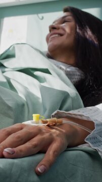 Brunette woman with hand IV listens to doctor as lies in bed