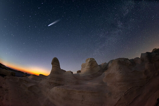 View of Sarakiniko Beach with unique white volcanic rock formations under a starry night sky with a comet visible in Milos, Greece.