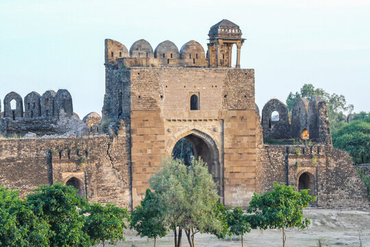 View of the historic Rohtas Fort with its massive stone walls, arched gateway, and battlements surrounded by green trees in Dina, Punjab, Pakistan.