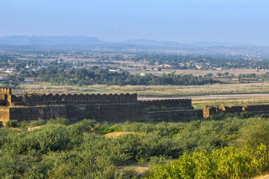 View of the historic stone battlements of Rohtas Fort surrounded by lush green vegetation and vast plains in Dina, Punjab, Pakistan.