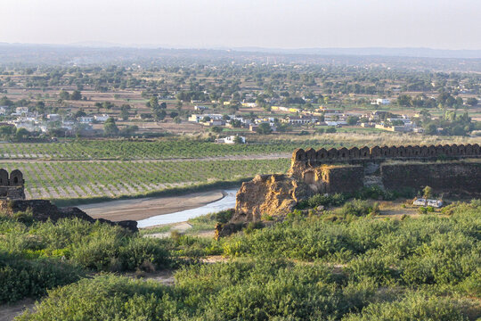 View of the historic stone walls of Rohtas Fort overlooking a winding stream, agricultural fields, and a distant town in Dina, Punjab, Pakistan.