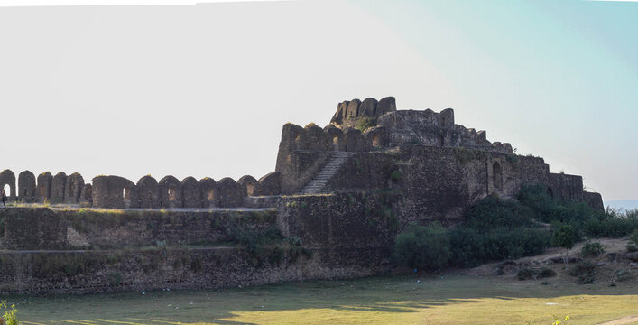 View of the historic Rohtas Fort with its ancient stone walls, arched battlements, and stairs rising above the grassy landscape in Dina, Punjab, Pakistan.