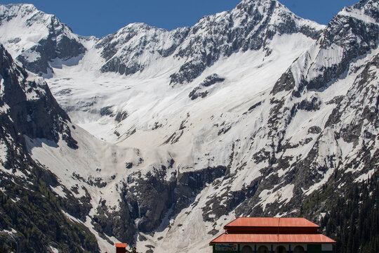 View of the Jahaz Banda Alpine Rest House nestled against the backdrop of towering snow-capped mountains in the Kumrat Valley, Khyber Pakhtunkhwa, Pakistan.