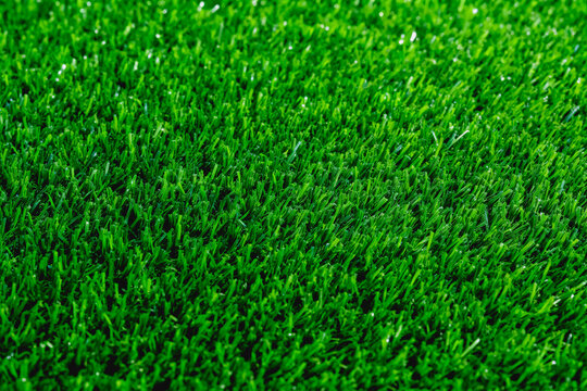 A close-up shot of dense, vibrant artificial green turf, showing fine synthetic grass blades and uniform texture. Suitable for use as a background or surface material.