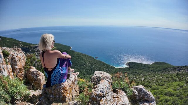 Woman on cliff enjoying panoramic view of sparkling Adriatic Sea and the Sveti Ivan Beach below. Exploring beautiful nature of Cres Island in Croatia. starting point to Sveti Ivan or Lubenice Beach