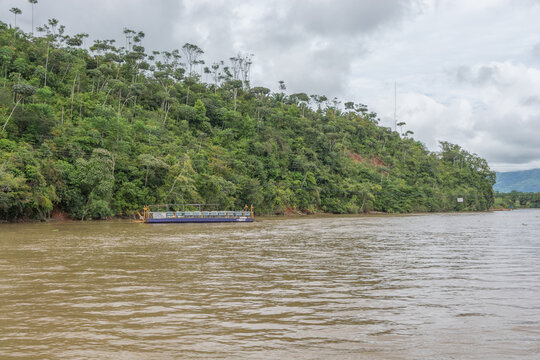 View of a small ferry boat navigating the Sierpe River, surrounded by dense tropical rainforest and lush green hills under a cloudy sky in Puntarenas Province, Costa Rica.