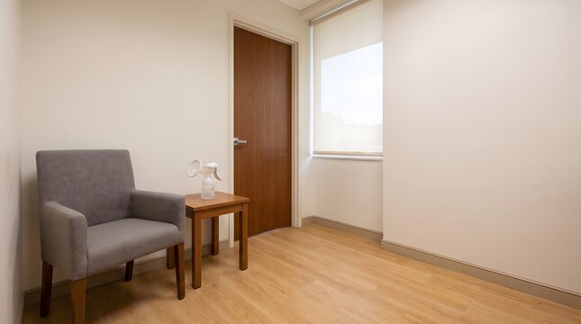 Small workplace lactation room with a chair, side table, breast pump, closed door and generous blank wall space for employee pumping support and privacy.