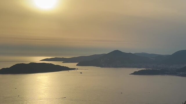 A beautiful view on Adriatic sea and Budva resort on sunset, Montenegro. Golden sunset over calm coastal bay with silhouetted islands, mountainous shoreline, and shimmering sunlight across tranquil
