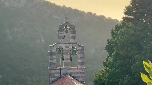 A beautiful view on Gradiste Monastery Church bell tower, Orthodox complex, Buljarica, Montenegro. Stone church bell tower framed by forested mountain slopes in warm evening light, tranquil